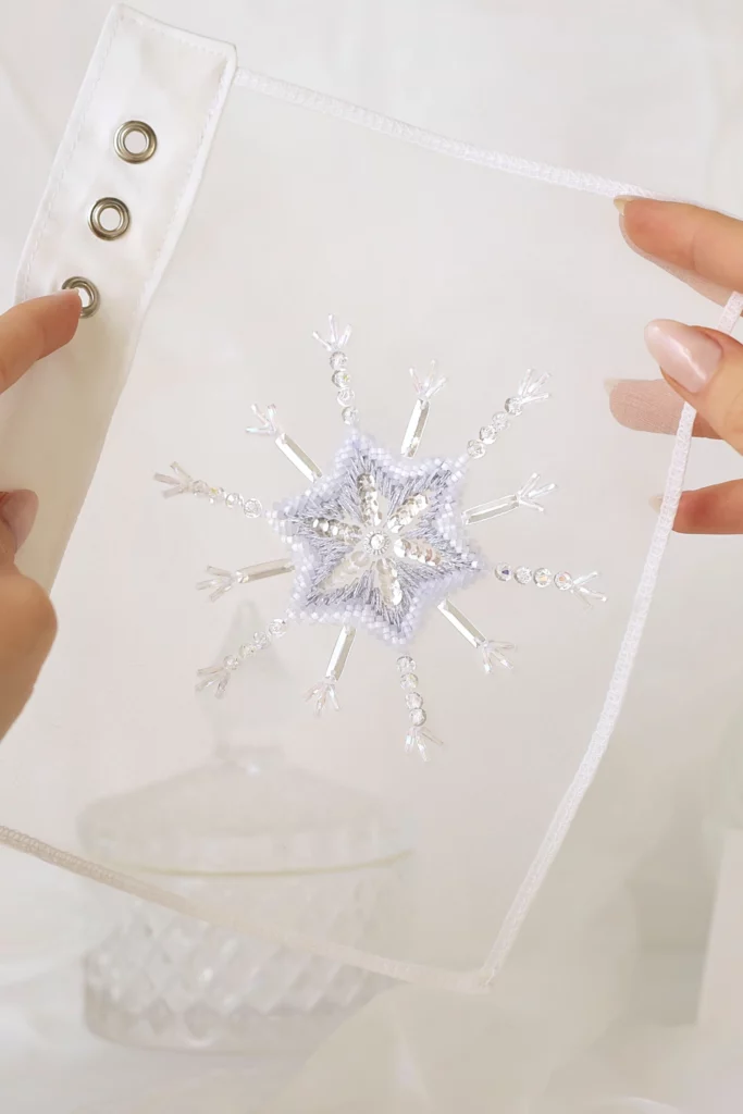 A handcrafted snowflake embroidery, Bianca, held in hands, showcasing its intricate details and winter-inspired elegance.