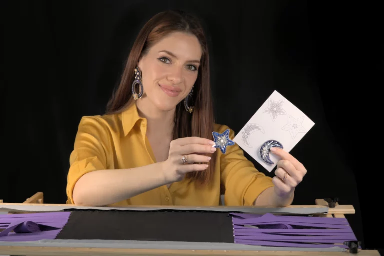 Laura S. Urbina présente des broches brodées d'étoile et de lune derrière un métier à broder, pour illustrer ses cours en ligne de broderie Haute Couture et Broderie d’Art.