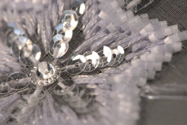 Macro prise de vue d'un patron de broderie raffiné de flocon de neige, mettant en valeur le délicat travail de perles et le savoir-faire de la Haute Couture.