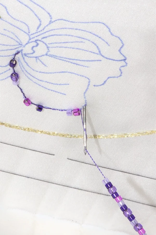 Close-up of Haute Couture embroidery using a Lunéville hook, beading delicate pearls onto fabric with precision and craftsmanship.