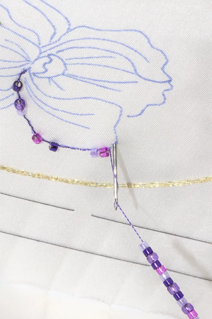 Close-up of Haute Couture embroidery using a Lunéville hook, beading delicate pearls onto fabric with precision and craftsmanship.