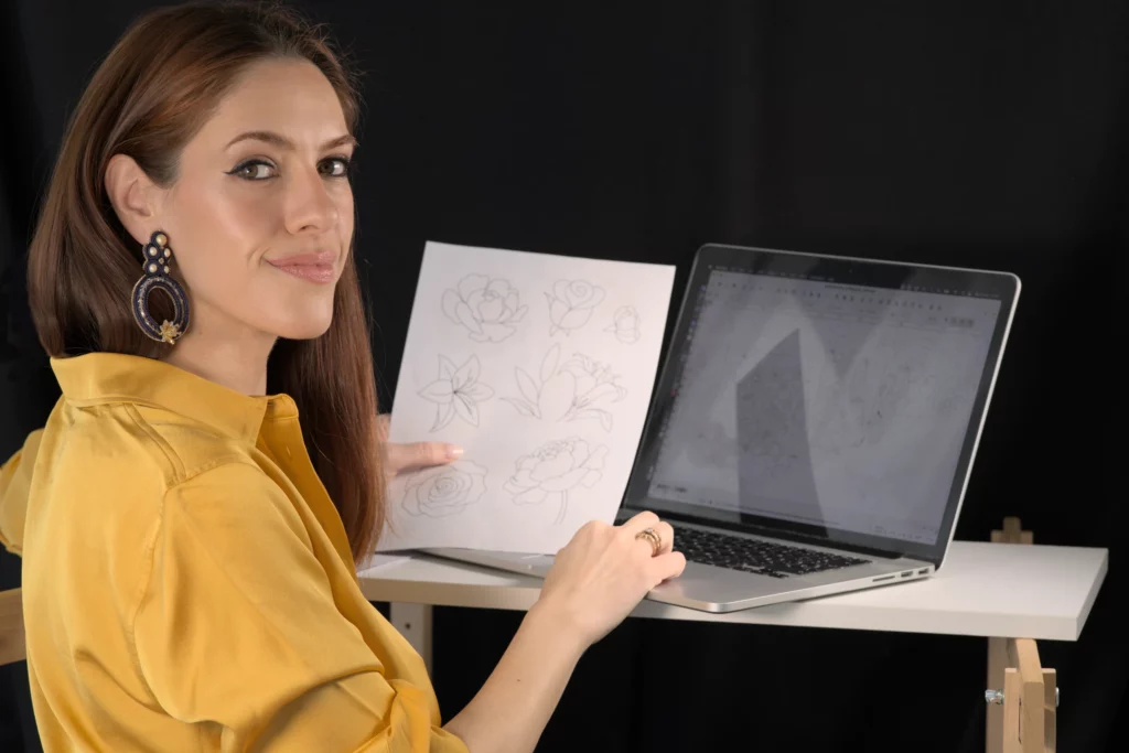 Laura S. Urbina presenta un diseño de bordado impreso en su ordenador, mostrando su servicio de diseño de bordado digital personalizado.