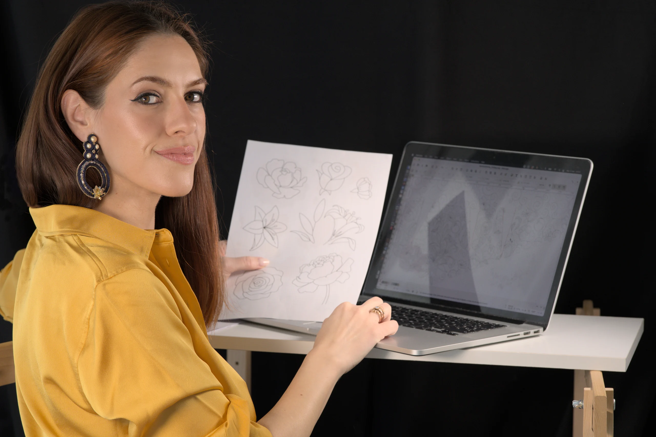 Laura S. Urbina presenta un diseño de bordado impreso en su ordenador, mostrando su servicio de diseño de bordado digital personalizado.