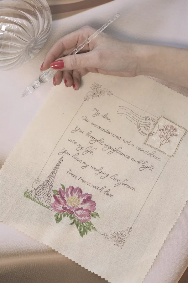A handcrafted embroidered love letter, From Paris with love, held in hands, featuring vintage details and the Eiffel tower.