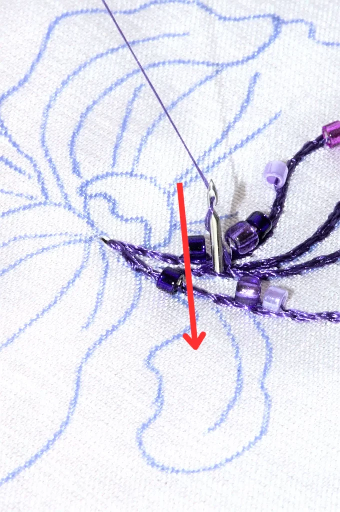 Gros plan sur la broderie au crochet de Lunéville avec des perles et des flèches rouges soulignant les conseils de Laura S. Urbina pour maîtriser les points et les techniques difficiles.