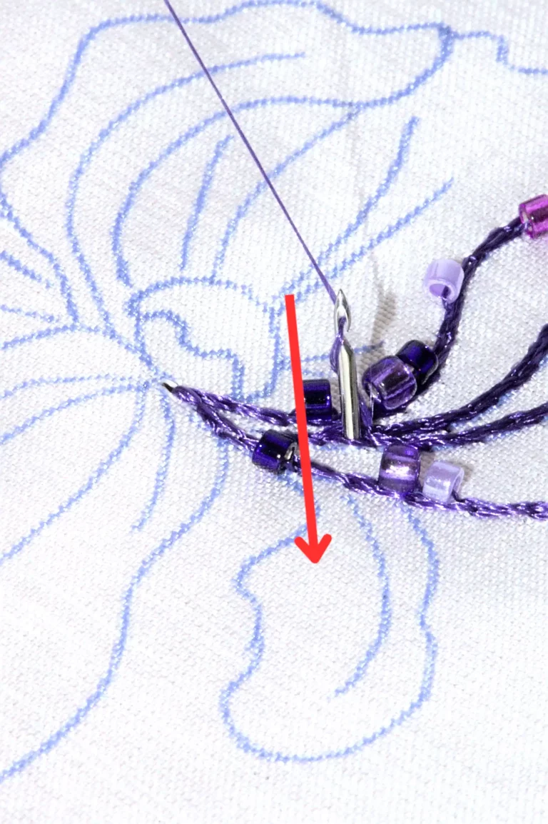 Gros plan sur la broderie au crochet de Lunéville avec des perles et des flèches rouges soulignant les conseils de Laura S. Urbina pour maîtriser les points et les techniques difficiles.