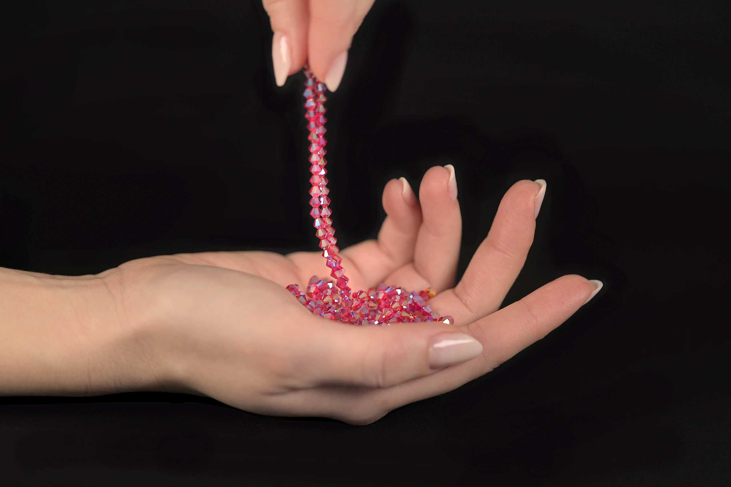 Primer plano de las manos de Laura S. Urbina sosteniendo lujosos cristales Swarovski para bordar, que representan la excelencia en la artesanía y el arte textil de alta calidad.