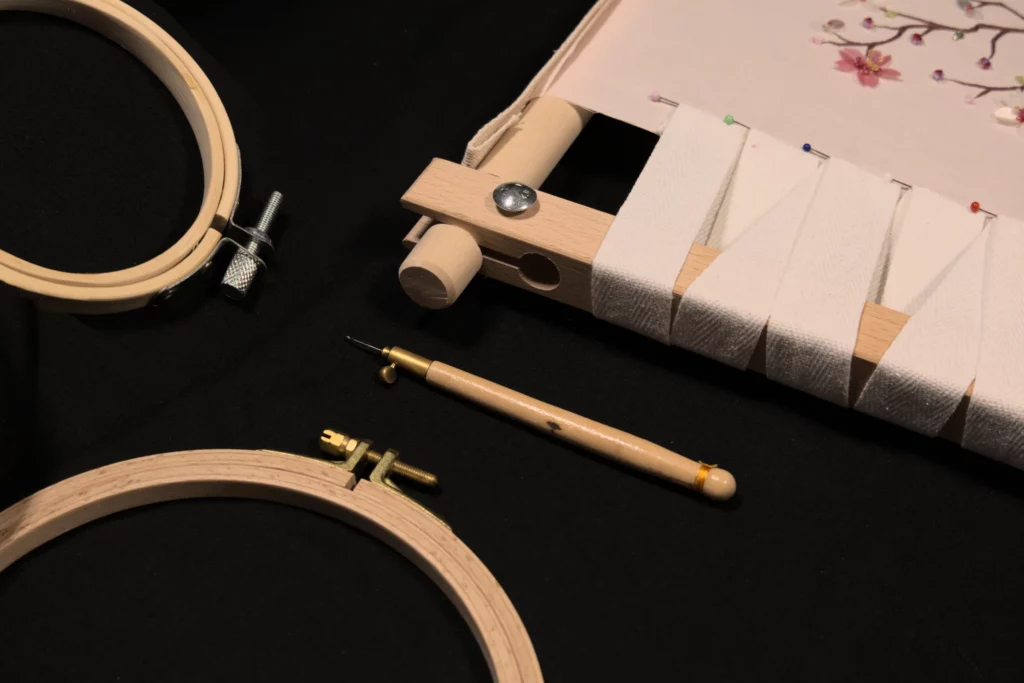 Représentation à plat des outils de broderie essentiels à la Haute Couture, notamment le métier à broder, le tambour et le crochet de Lunéville pour une broderie de précision.