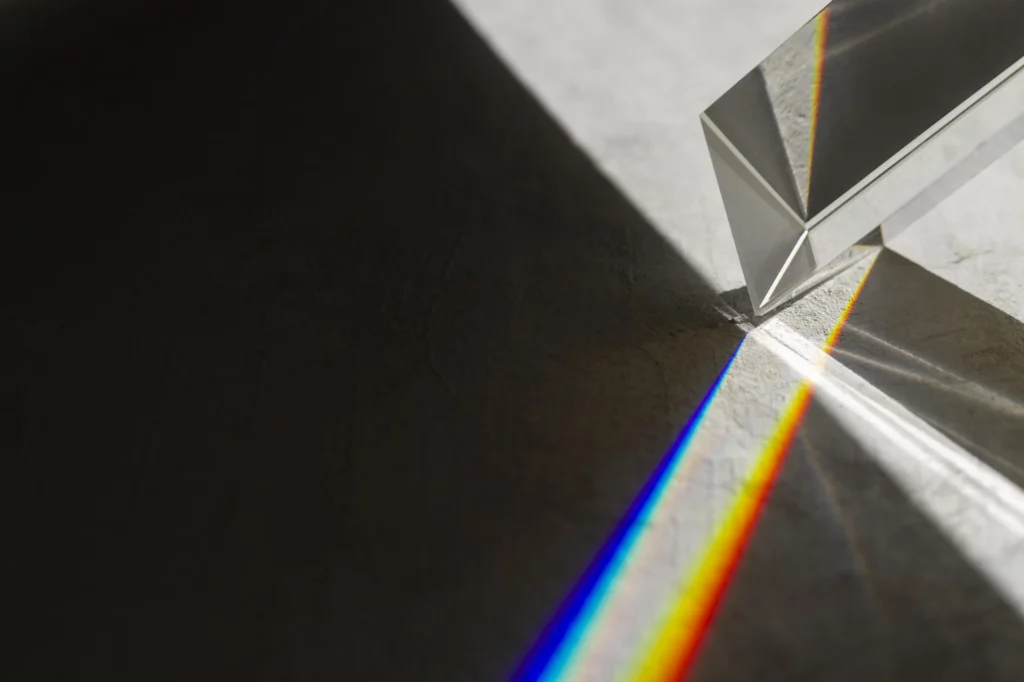 A light beam refracts through a glass prism into a spectrum of rainbow colors on a dark background.