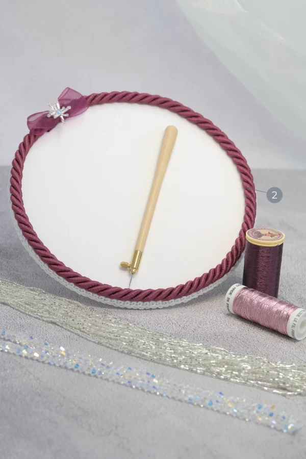 Fuchsia Starlight embroidery beading plate holding a Lunéville hook, metallic threads, beads, and crystals for couture embroidery.