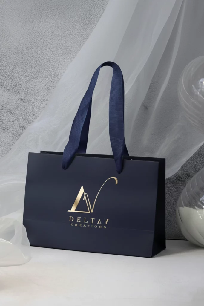 Elegante bolsa de compra de lujo azul medianoche con logo Delta V Créations dorado, acompañada de decoración de cristal.