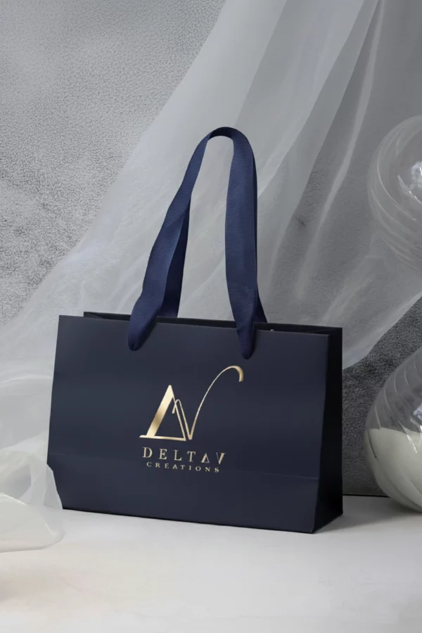 Elegant Delta V Créations navy blue luxury shopping bag with gold logo, accompanied by a refined glass décor.