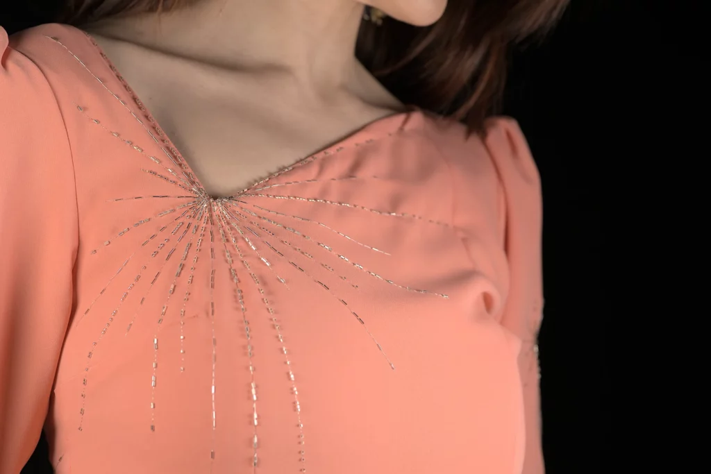 Primer plano de un bordado en forma de rayos de sol integrado a la perfección en las costuras de una prenda, realzando el diseño con un excelente trabajo artesanal.