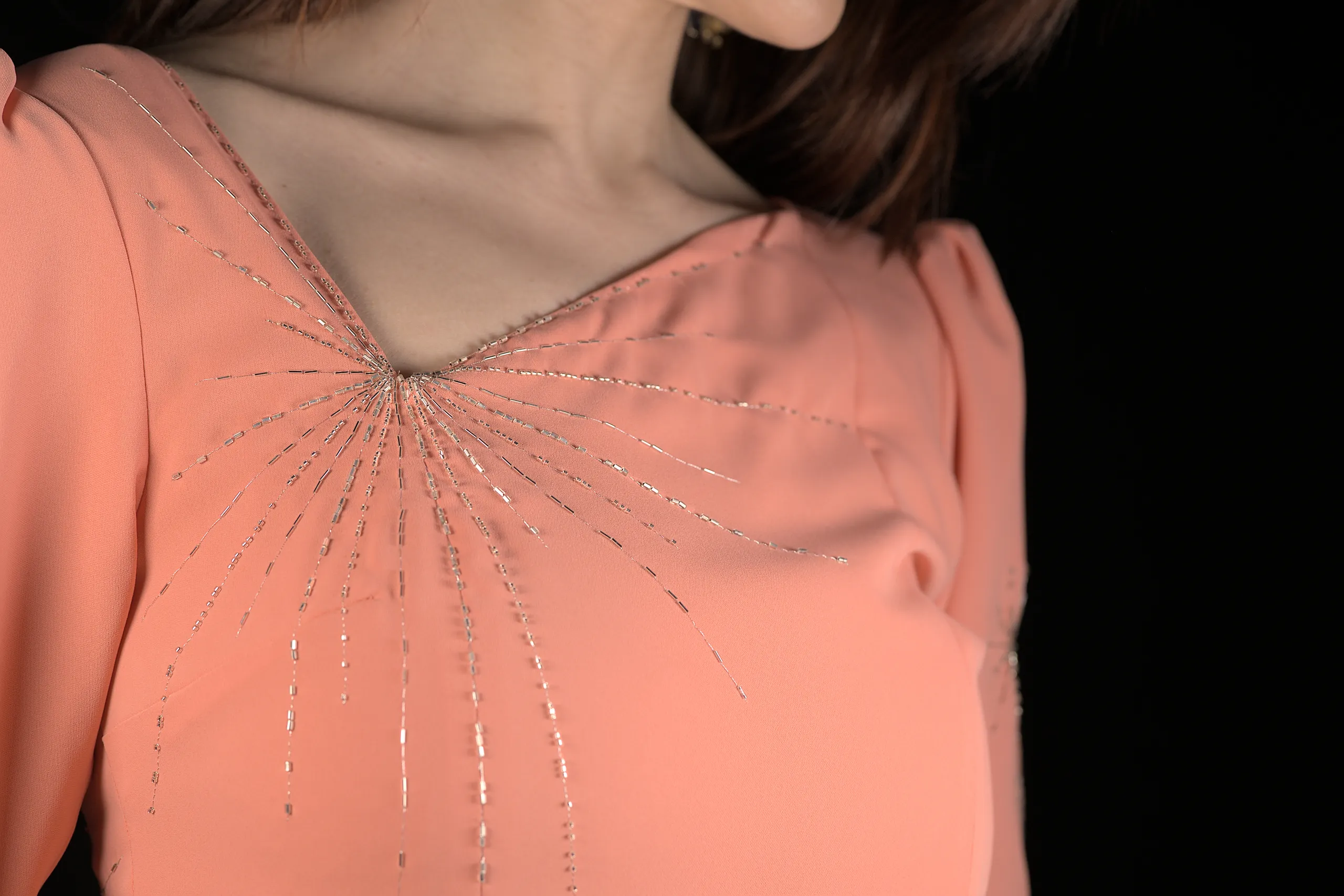Primer plano de un bordado en forma de rayos de sol integrado a la perfección en las costuras de una prenda, realzando el diseño con un excelente trabajo artesanal.