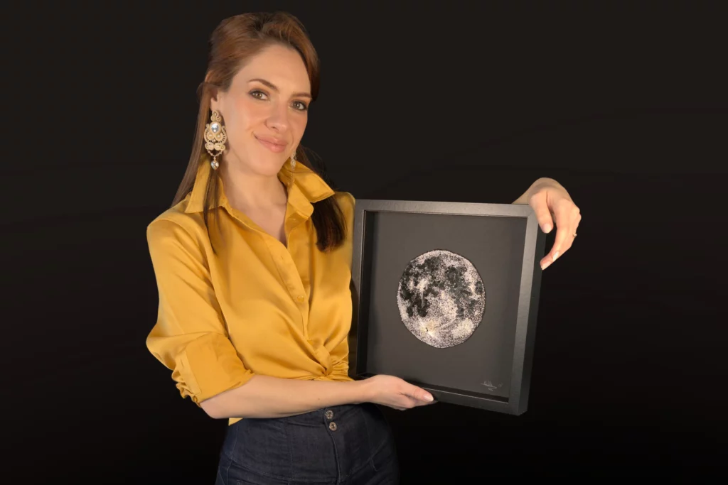 Laura S. Urbina holding a fully hand-embroidered artwork of the Moon, showcasing bespoke embroidery and artistic textile design.