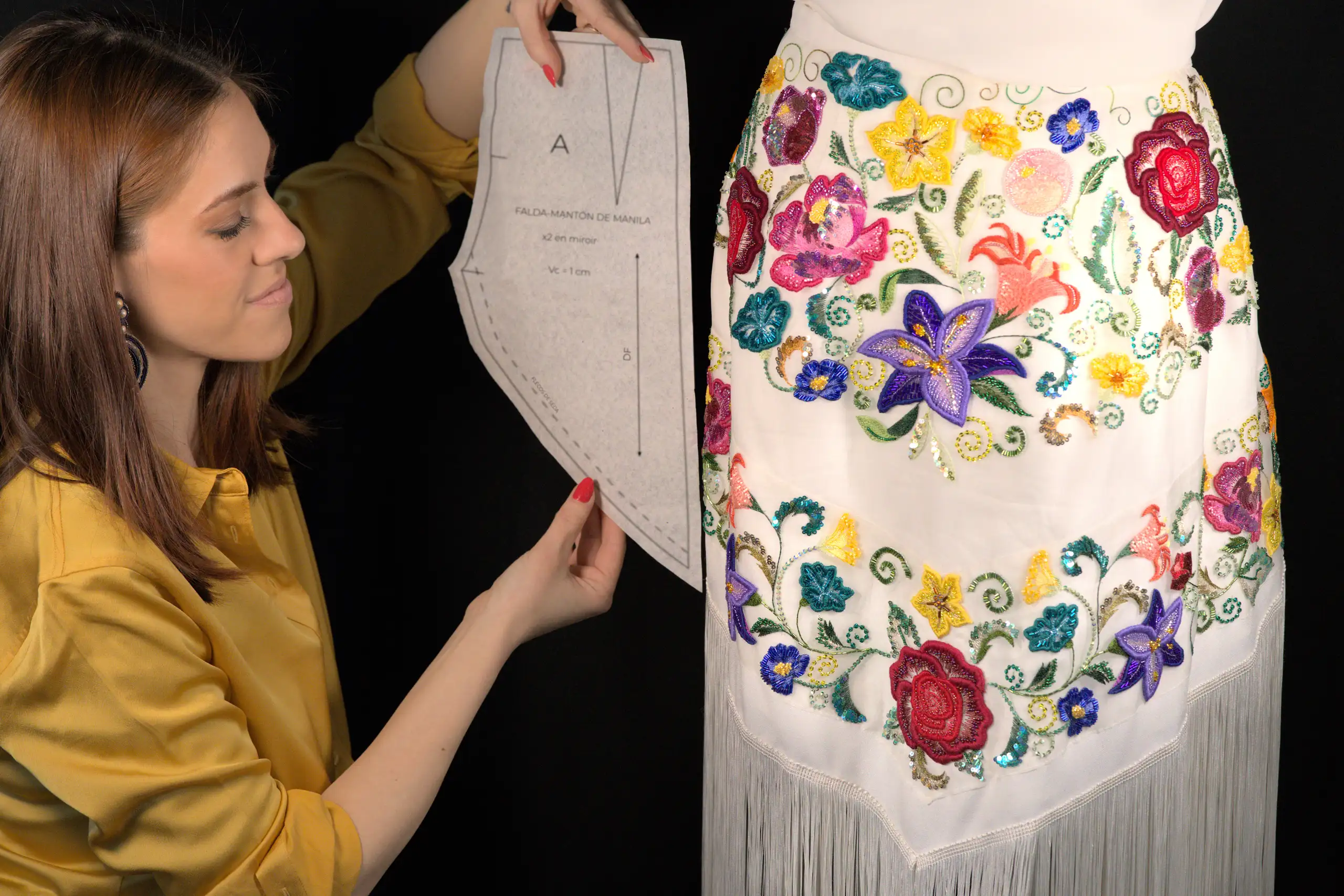 Laura S. Urbina de pie junto a un maniquí de costura cubierto con un patrón de alta costura, ofreciendo servicios de bordado a medida para diseñadores de moda.