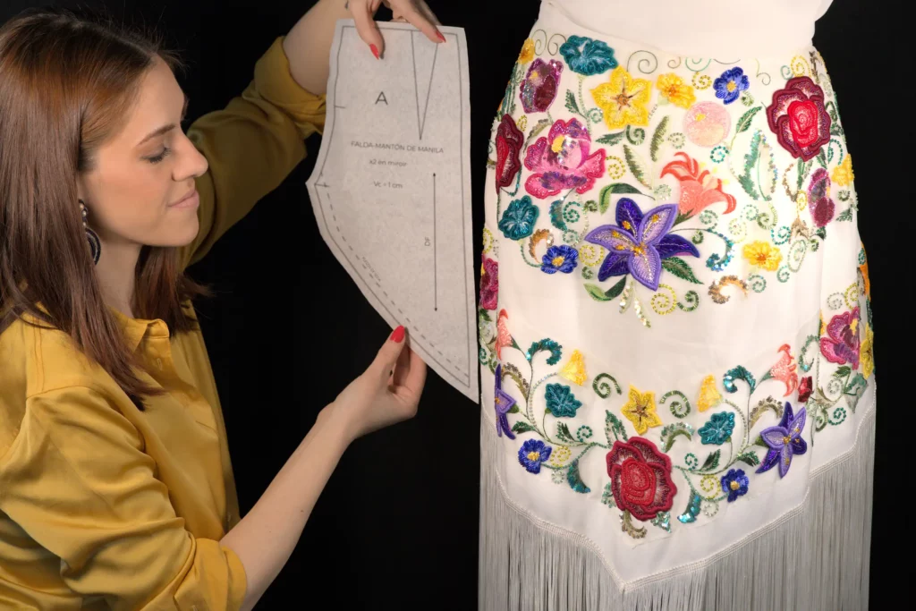 Laura S. Urbina standing beside a sewing mannequin draped with a couture pattern, offering bespoke embroidery services for fashion designers.