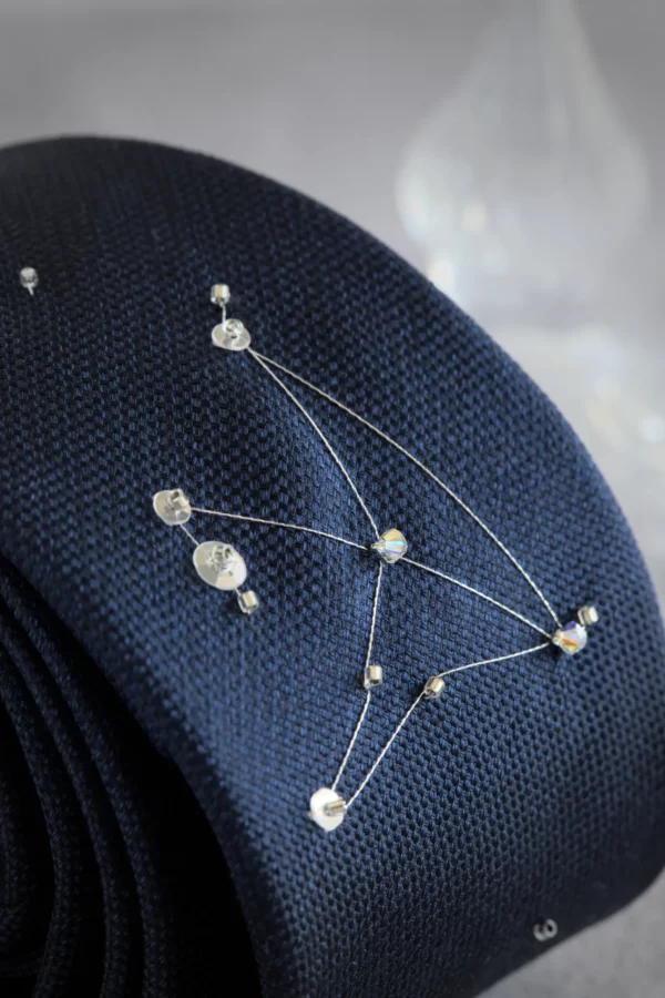Detailed embroidery of Aquila constellation with silver thread and shimmering crystals on navy silk necktie.