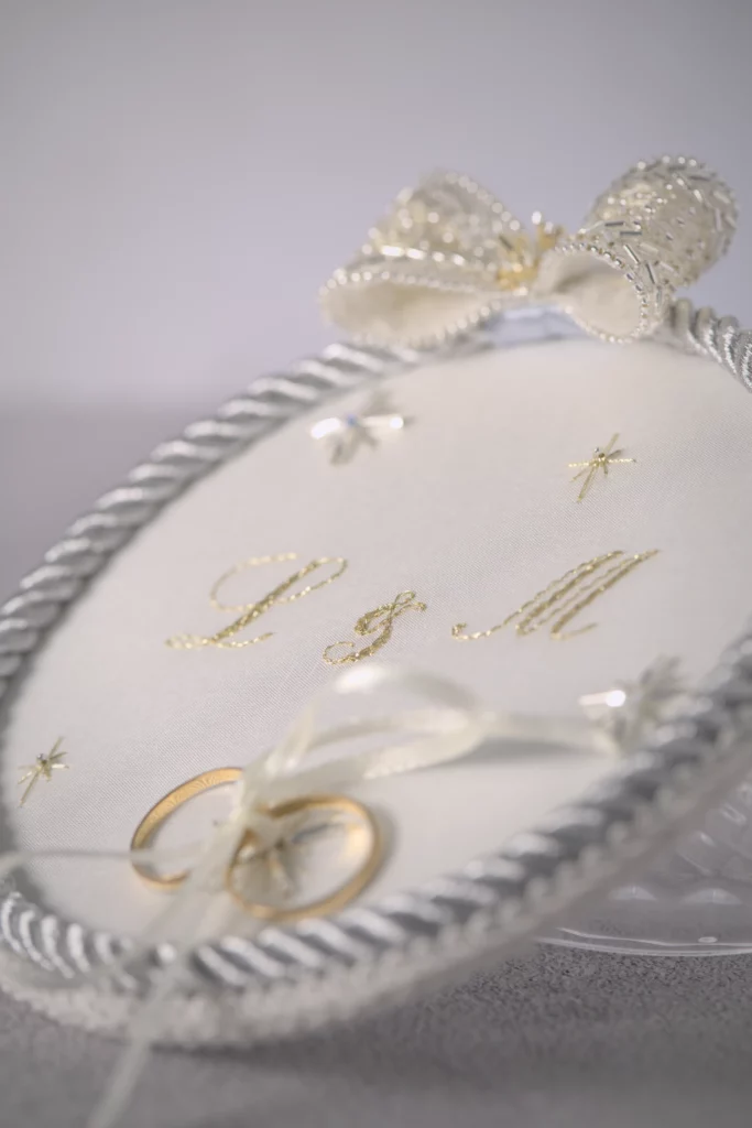 Porta alianzas ASTRA personalizado con iniciales L & M bordadas, estrellas de cristal y alianzas atadas con satén, con temática espacial y estelar.