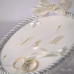 Personalized ASTRA wedding ring holder with embroidered initials L & M, crystal stars, and satin-tied wedding bands in a space and star theme.