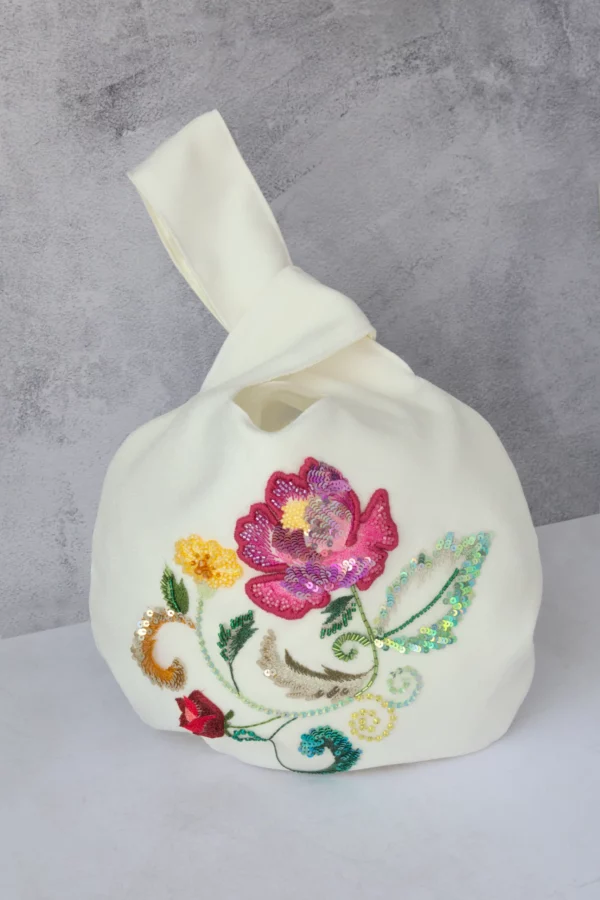 Full view of Carina Japanese knot bag in off-white crêpe, with multicolored floral embroidery and artisanal detailing. Handcrafted in France.