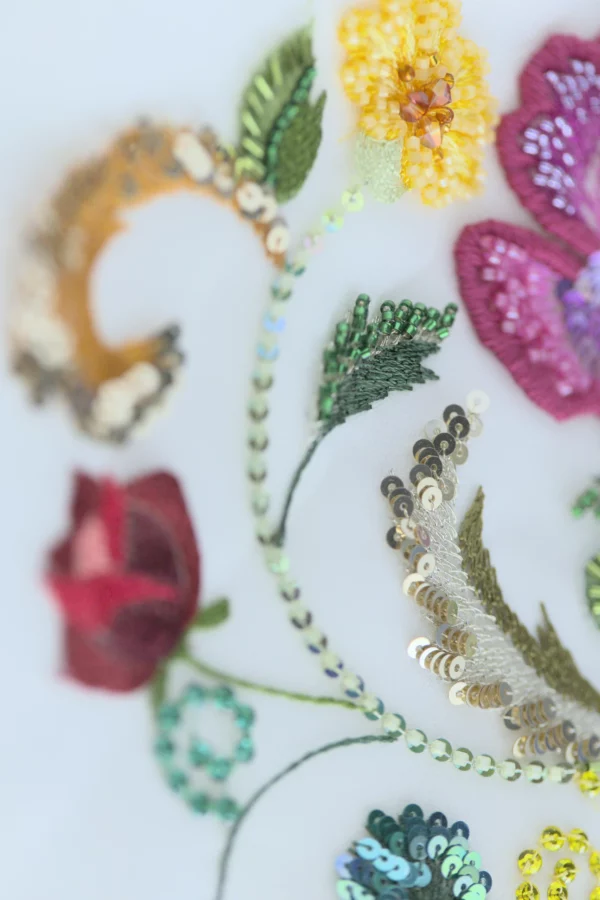 Close-up of Carina bag’s floral embroidery with sequins, silk threads, and beads on crêpe. Vibrant handcrafted details in radiant colors.
