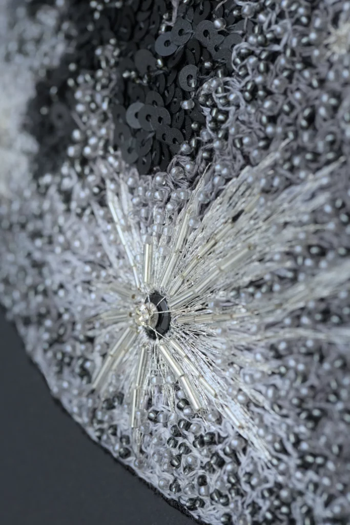 Close-up of hand-embroidered lunar surface with crystals, sequins and silver thread, revealing rich texture and luxurious detail.