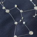 Détail brodé de la constellation d’Orion en fil argenté et cristaux sur cravate de soie marine, évoquant un ciel étoilé raffiné.