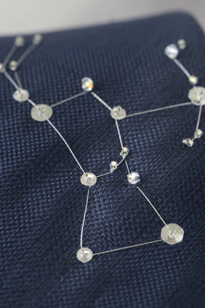Détail brodé de la constellation d’Orion en fil argenté et cristaux sur cravate de soie marine, évoquant un ciel étoilé raffiné.
