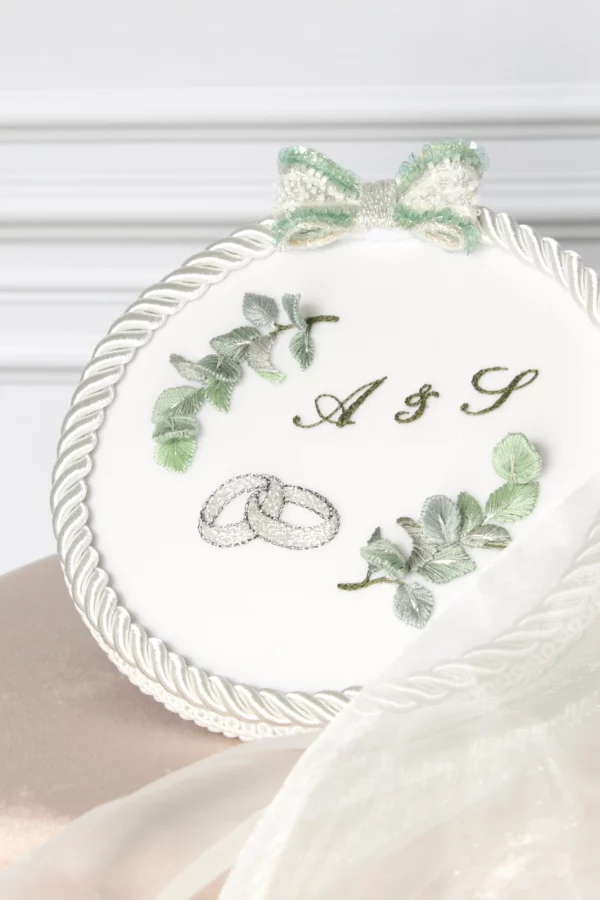 Personalized wedding ring holder with custom vegetal embroidery, the couple’s initials and two intertwined rings.