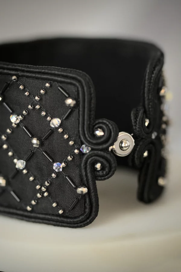 Gros plan de la manchette noire brodée de cristaux, mettant en valeur l'élégante grille brodée et la fermeture à pression discrète de cette création de luxe made in France.