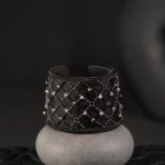 A black embroidered crystal cuff is presented on a concrete display stand, highlighting the know-how of french couture embroidery in a timeless and elegant creation.