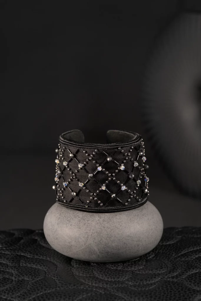 Une manchette en cristal brodée noire est présentée sur un socle en béton, mettant en valeur le savoir-faire de la broderie haute couture française dans une création intemporelle et élégante.