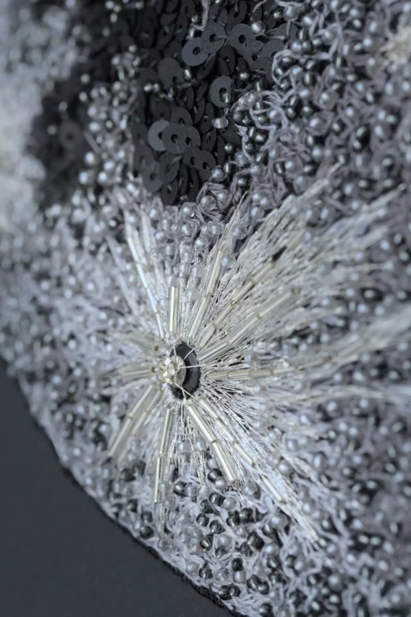 Gros plan sur la surface lunaire brodée à la main avec cristaux, paillettes et fils argentés, dévoilant une texture luxueuse raffinée.