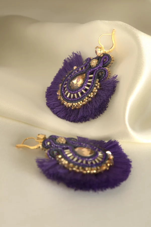 Par de pendientes boho chic bordados a mano en violeta y oro, con cristal y pompones de algodón, sobre seda color crema.