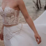 Bespoke bridal embroidery on the Hestia gown, golden flames and geometric belt details against a sandy blurred background.