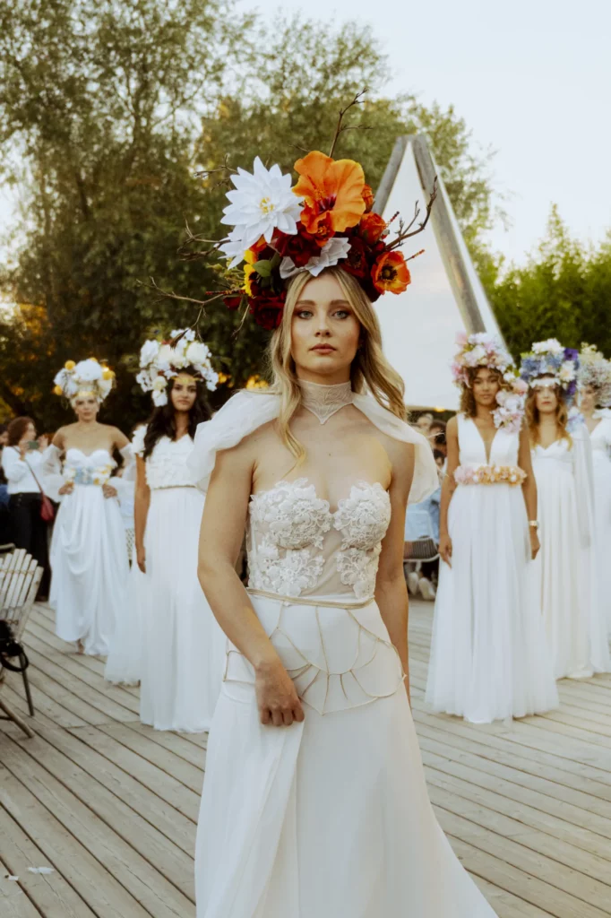 Model wearing bespoke bridal embroidery Hestia gown with golden neck and skirt pieces, brides blurred in background.