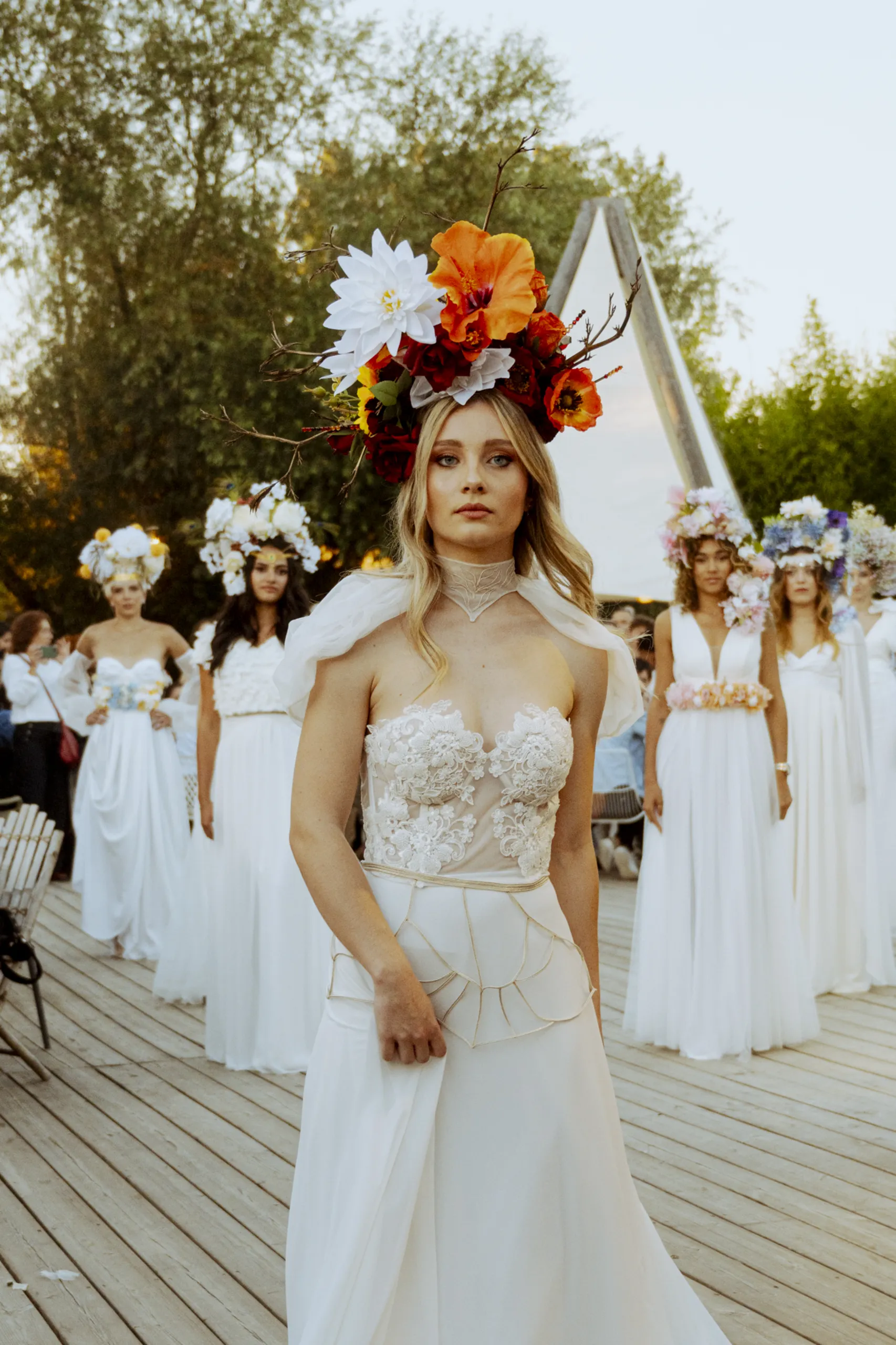 Modelo con vestido Hestia y bordados nupciales personalizados en cuello y falda, con otras novias difuminadas detrás.