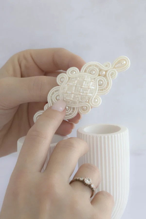 Hands holding the bridal hair clip Meissa, hand-embroidered with pearls and crystals, elegant wedding hair accessory.