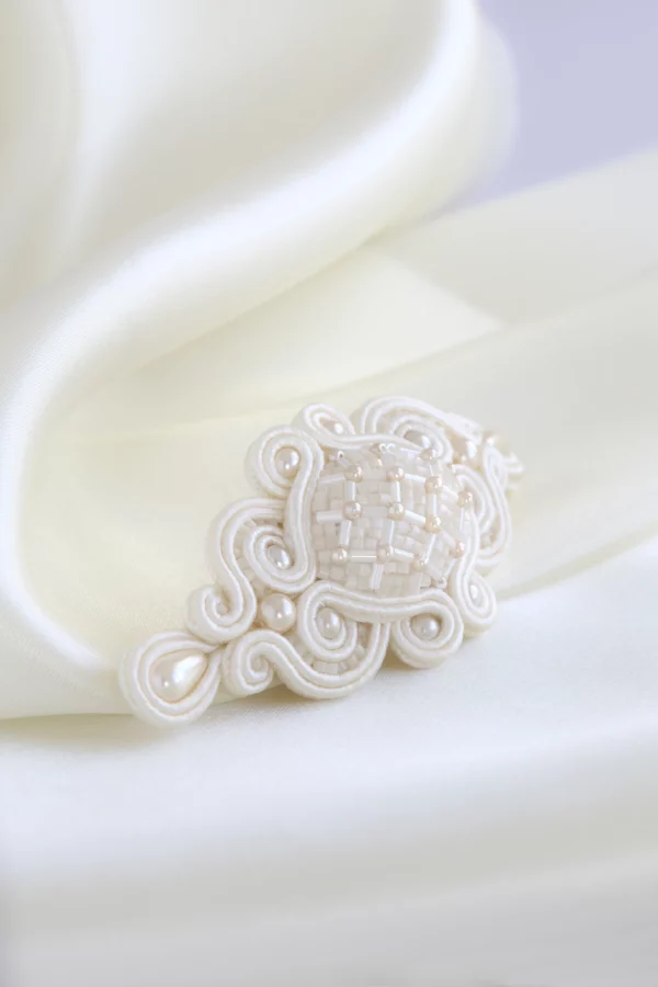 Hand-embroidered bridal hair clip Meissa placed over smooth silk fabric, elegant wedding hair accessory.