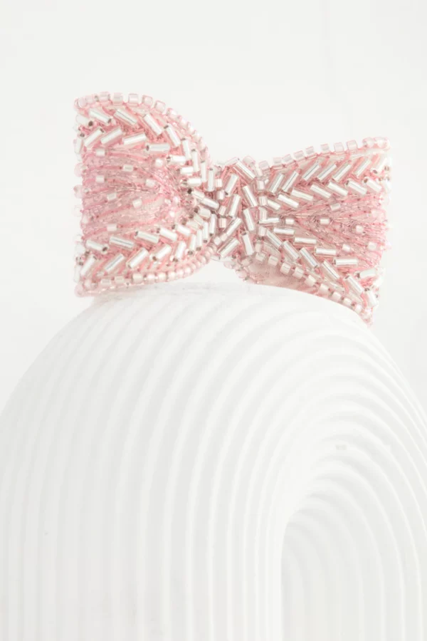 Primer plano de un broche lazo rosa Venus sobre columna de cemento blanco, bordado a mano en organza de seda y cuentas.