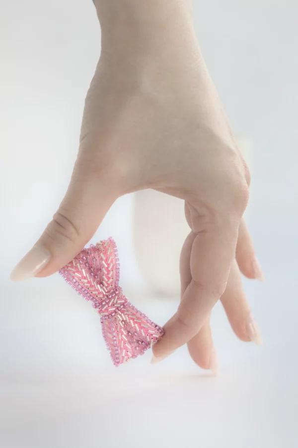 Mano elegante sosteniendo un broche lazo rosa Venus sobre fondo de mármol blanco, joya bordada de resiliencia.