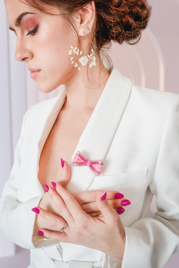 Modelo luciendo el broche lazo rosa Venus sobre un blazer blanco, accesorio bordado a mano, símbolo de fuerza y elegancia femenina.