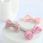 Tres broches lazo rosa Venus bordados a mano sobre mármol con columna griega, símbolo de fuerza femenina.