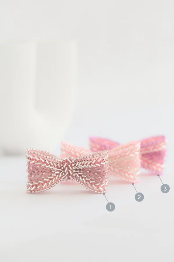 Série de trois variations de la broche ruban rose Venus sur marbre avec arrière-plan de colonne grecque, brodées en organza de soie.
