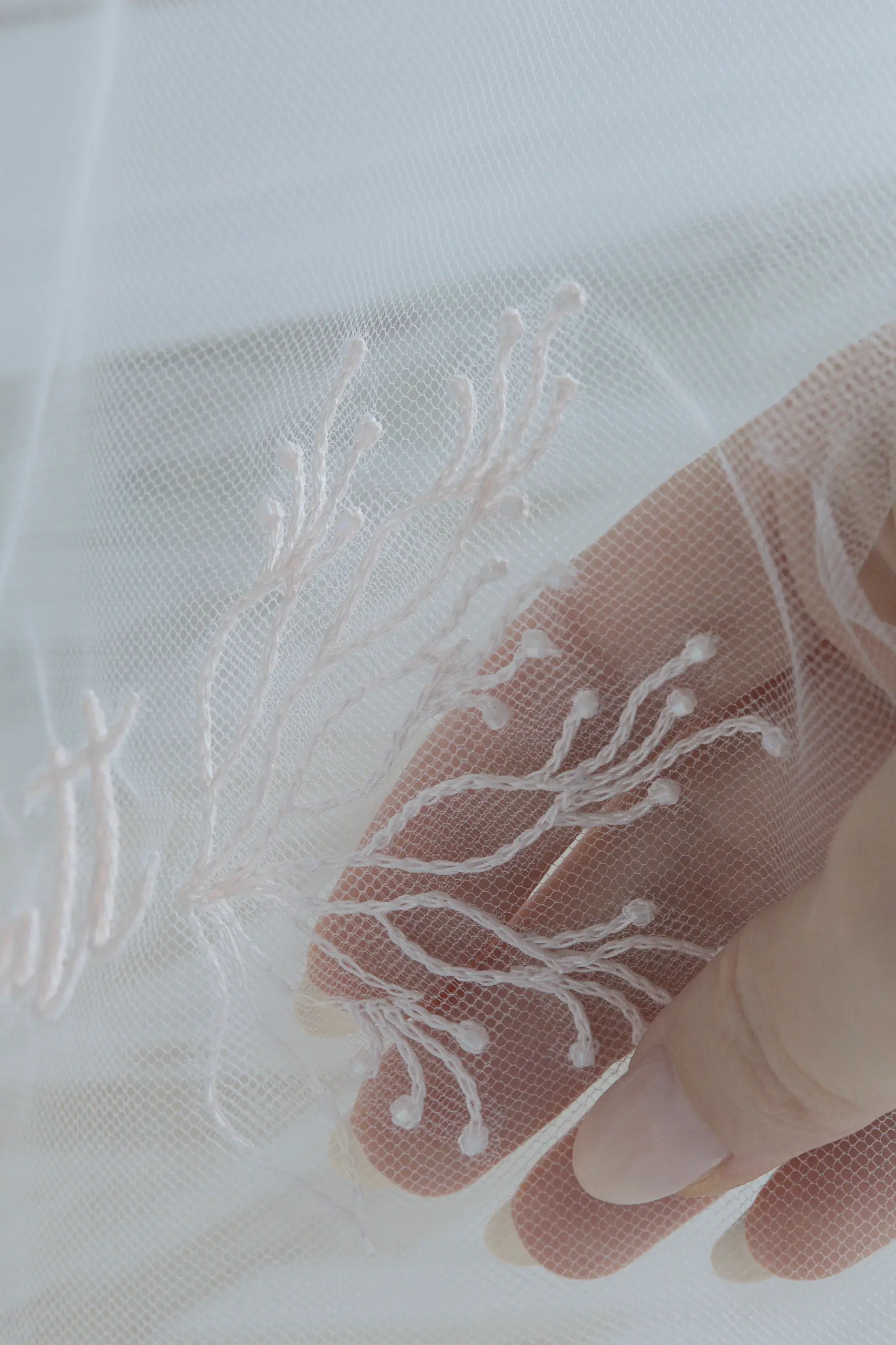 Primer plano del motivo de hojas bordado en un velo de novia, tul sostenido delicadamente con la mano.