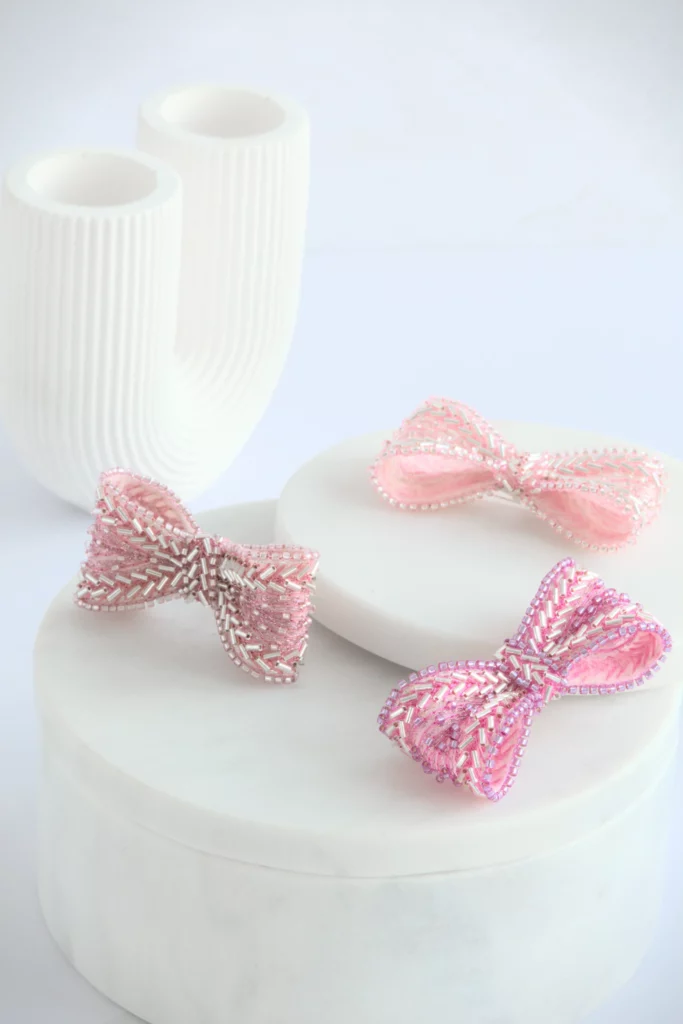 Three hand-embroidered Venus pink ribbon brooches on marble with Greek-inspired column prop, symbolizing feminine strength.