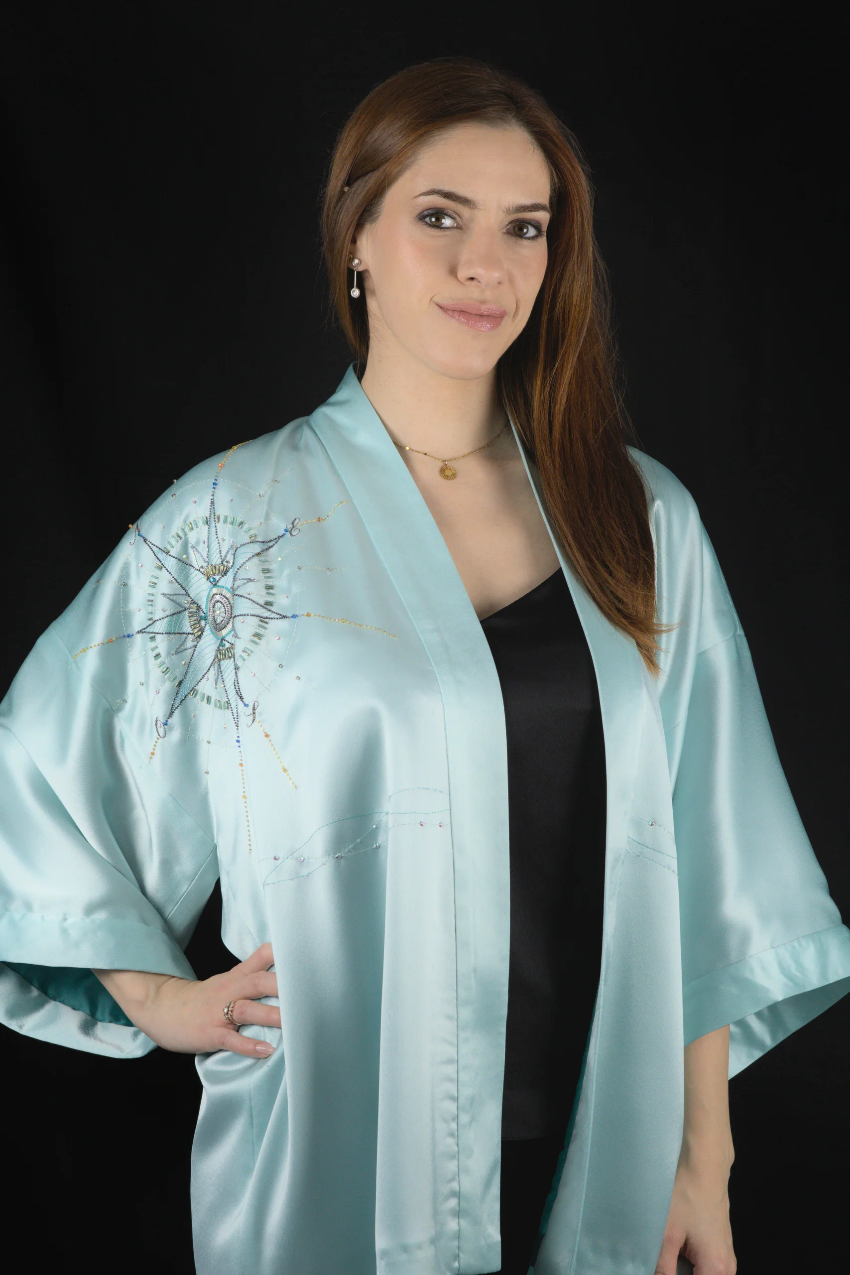 Model wearing the turquoise Alcyone kimono vest with its hand-embroidered compass rose on the front.