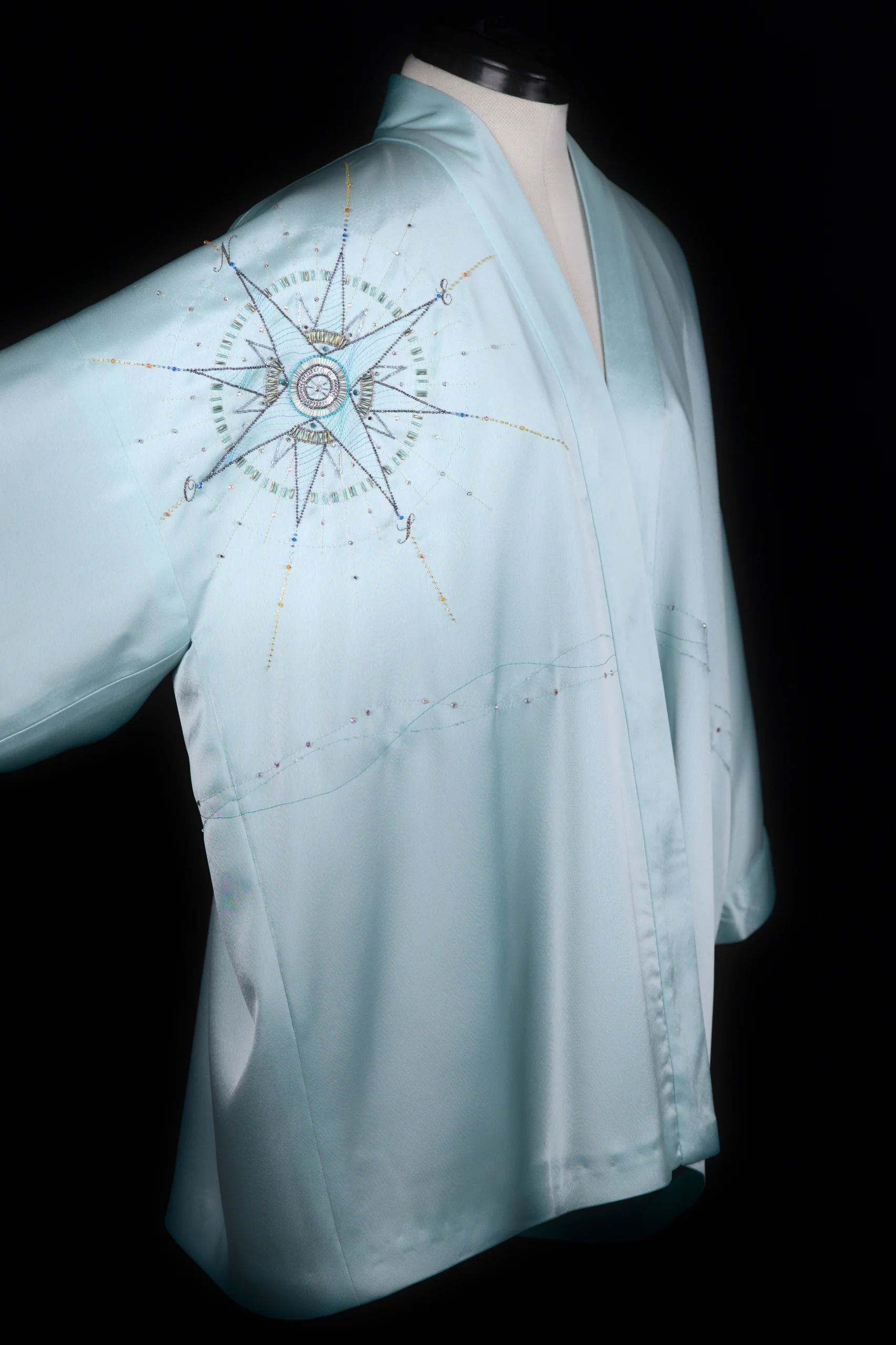 Mannequin wearing the turquoise Alcyone kimono vest, showing the hand-embroidered compass rose from a diagonal angle.