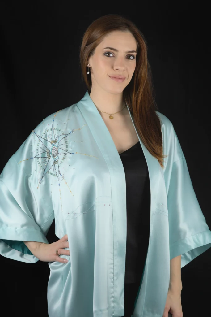 Model wearing the turquoise Alcyone kimono vest with its hand-embroidered compass rose on the front.